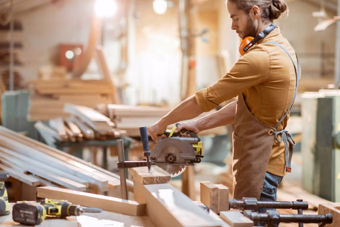 Carpenter cutting a clamped board with a circular saw in a wood shop