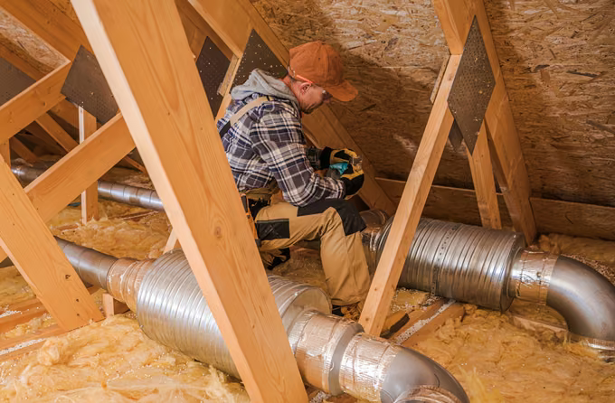 HVAC technician sealing insulated ductwork between roof trusses in an attic