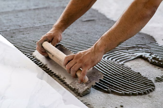 Tile setter spreading thinset with a notched trowel beside a laid marble tile