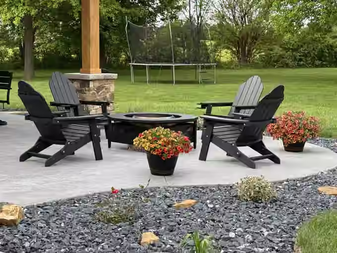 Landscaped backyard patio with four Adirondack chairs around a fire pit, planters, and a rock bed